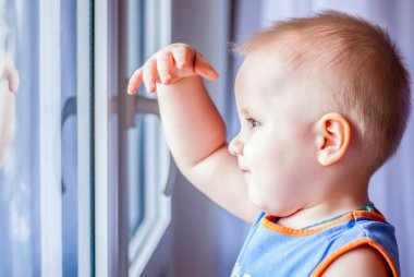 Çocuk pencereden dışarı bakıyor. Gerçekten yürümek istiyor. Karantina yüzünden herkes evde kalıyor ve hiçbir yere gitmiyor..