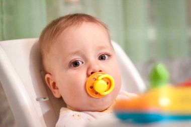 Yüksek sandalyede oyuncaklarla oynayan bir bebek. Ağzındaki emzik..