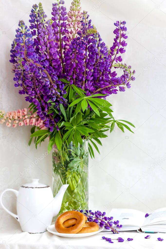  Sweet bagels and tender lupine flowers. Light composition with bright and purple flowers. A gentle and romantic morning with tea and a book. A book of poems for Breakfast.