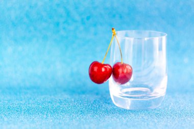 Tatlı kirazlar. Kırmızı kirazlar şeffaf bir bardağa asılır. Olgun çilek. Sunumlar ve grafik çalışmaları için parlak yaz arkaplanı.