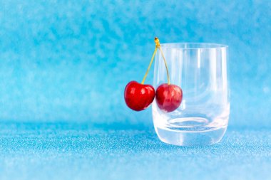 Tatlı kirazlar. Kırmızı kirazlar şeffaf bir bardağa asılır. Olgun çilek. Sunumlar ve grafik çalışmaları için parlak yaz arkaplanı.