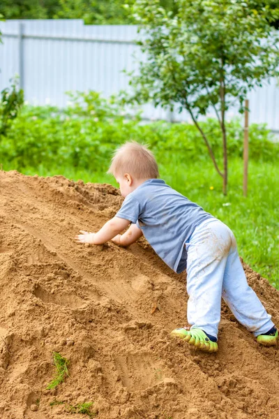 A little boy climbs a mountain with sand. The child is all dirty, but happy. Summer.
