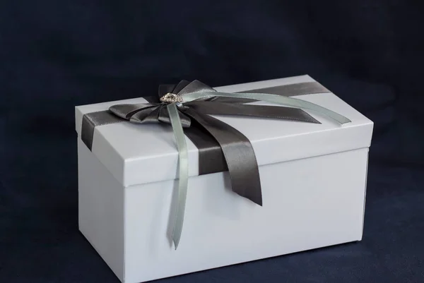 The gift box is white with a beautiful gray bow. Gift on a dark background. Holidays and surprises. Satin bows with rhinestones.