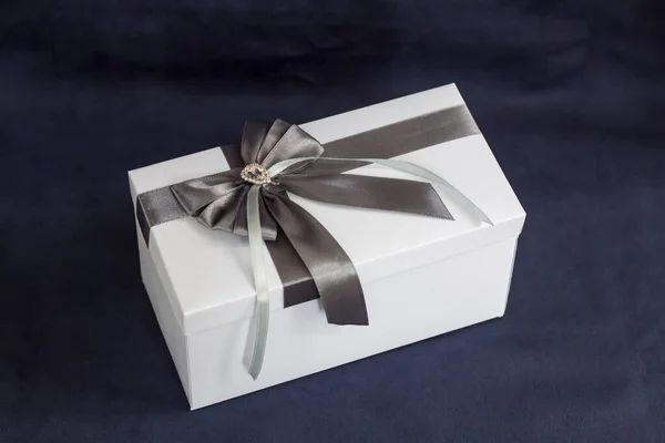 The gift box is white with a beautiful gray bow. Gift on a dark background. Holidays and surprises. Satin bows with rhinestones.