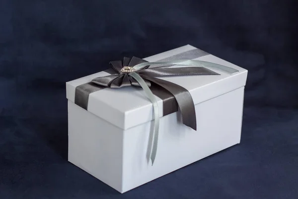 礼品盒是白色的 有一个漂亮的灰色蝴蝶结 在黑暗背景下的礼物 假期和惊喜 缎子弓和莱茵石 — 图库照片