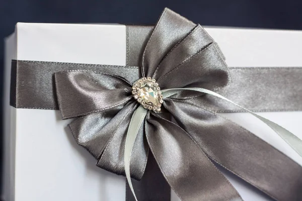 礼品盒是白色的 有一个漂亮的灰色蝴蝶结 在黑暗背景下的礼物 假期和惊喜 缎子弓和莱茵石 — 图库照片