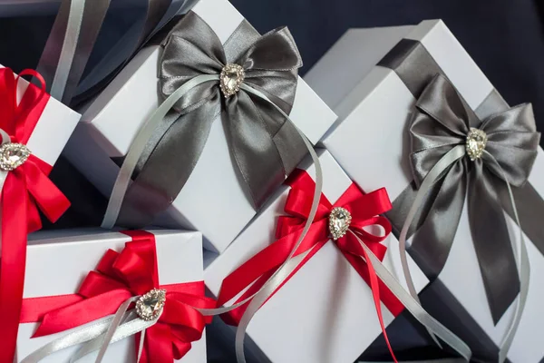 很多礼物礼品盒是白色的 有一个红灰相间的漂亮蝴蝶结 在黑暗背景下的礼物 假期和惊喜 缎子弓和莱茵石 — 图库照片