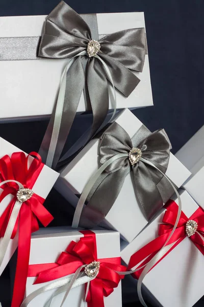 很多礼物礼品盒是白色的 有一个红灰相间的漂亮蝴蝶结 在黑暗背景下的礼物 假期和惊喜 缎子弓和莱茵石 — 图库照片