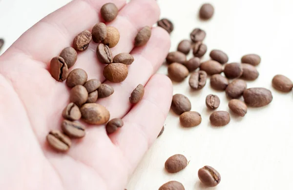 Roasted coffee beans on a wooden background. Coffee and light wood background. Grain in hand.