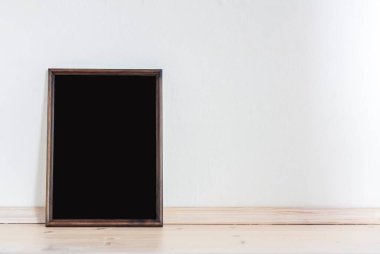 Koyu bir çerçeve, açık bir duvara karşı ahşap bir tezgahın üzerinde duruyor. Sunum tasarım elementleri. Eklenecek şablon.