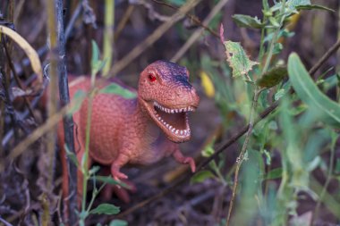 Çalılıktaki oyuncak dinozor doğal çevreyi taklit eder. Çocuklar için oyuncaklar.