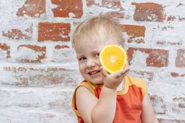 Çocuk portresi. Portakalla poz veren sevimli bir çocuk. Bir çocuğun duyguları. Duvara dayanmış bir çocuğun portresi..  