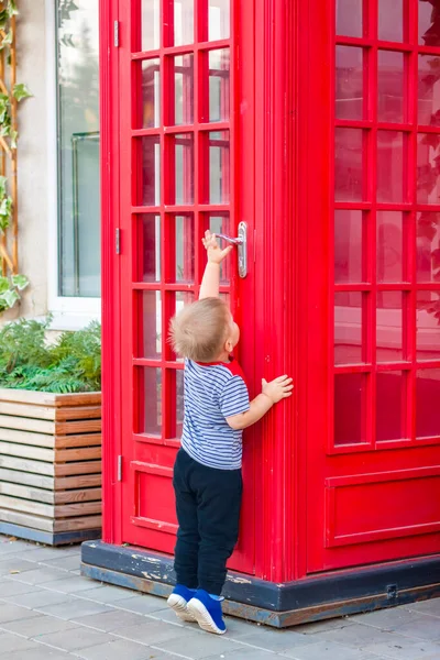 A little boy wants to enter a red phone booth. The red telephone box.