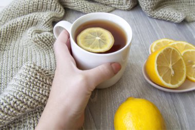 Limonlu zencefil çayı. Bir fincan çay bir kadının eliyle tutulur. Soğuk algınlığı ve enfeksiyon mevsimi. Bağışıklığın güçlenmesi. Sıcak bir eşarpla limonlu ve zencefilli bir fincan çay..
