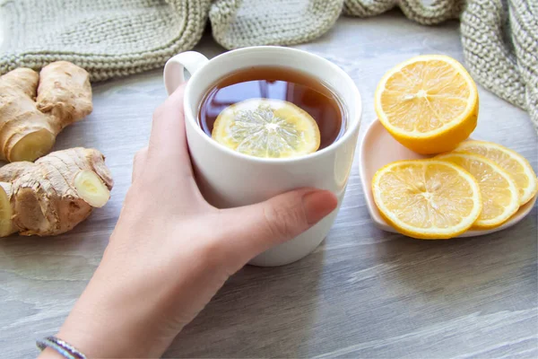 Ginger tea with lemon. A Cup of tea is held by a woman\'s hand. Season of colds and infections. Strengthening of immunity. A Cup of tea with lemon and ginger in a warm scarf.