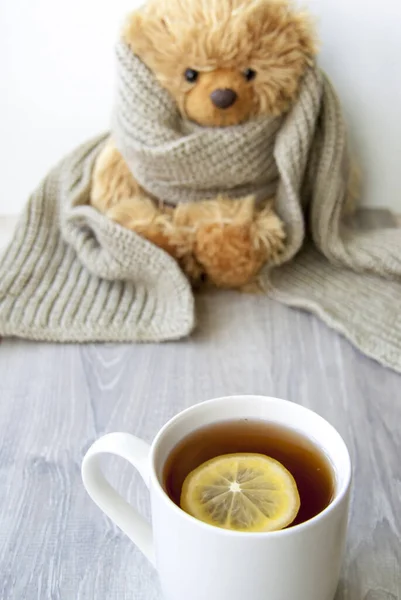 Ginger tea with lemon. Season of colds and infections. Strengthening of immunity. A Cup of tea with lemon on the background of a toy bear in a warm scarf.