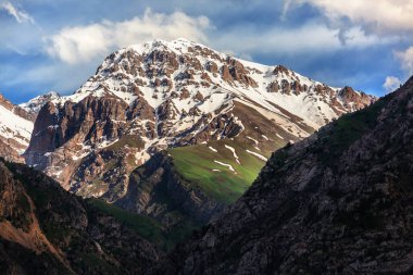 Dağların ve yeşil ağaçların arka planında güzel bir gökyüzü. Dağlık arazinin dağ manzarası. Dağın tepesinde kayalar ve karlar var.