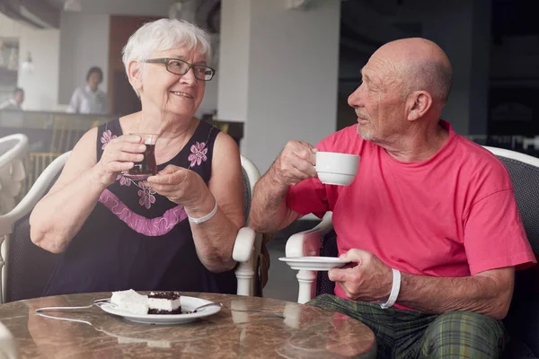 Portrait of happy senior couple laughing ,enjoying dinner together, drinking beverages with cakes in lobby bar of modern hotel. Smiling and talking, spending great holiday time abroad. Film effect.