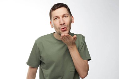 Hoş dudaklar hava öpücük Sevgiliye, darbeler gibi görünüyor büyük bir sevgi ve sempati ile rahat haki tişört turlarda karanlık büyüleyici gözlü esmer erkek arayanlar, flört etmeye çalışır izole beyaz stüdyo duvarda