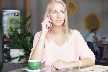 Teknoloji ve iletişim kavramı. Akıllı telefon, popüler modern kafede ücretsiz vakit erkek arkadaşıyla konuşurken headshot olan şık mavi gözlü sarışın kadın trendy saç kesimi, yana doğru görünüyor.