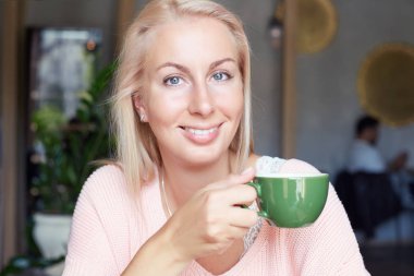 İyi görünümlü neşeli sarışın Amerikan kadın kırpılmış shot yeşil fincan kahve tutar, rahat kafeteryada öğle yemeği vardır, gezi, yabancı ülkede oluşturduğu olumlu duygular ifade eder sonra aittir.