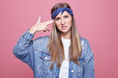 Çekici sıkılmış genç bayan portresi Tapınağı'nda parmak tutar, intihar süsü, trendy var. saç modeli, şık denim içinde giyinmiş pozlar pembe arka plan boş kopya alanı ile karşı.