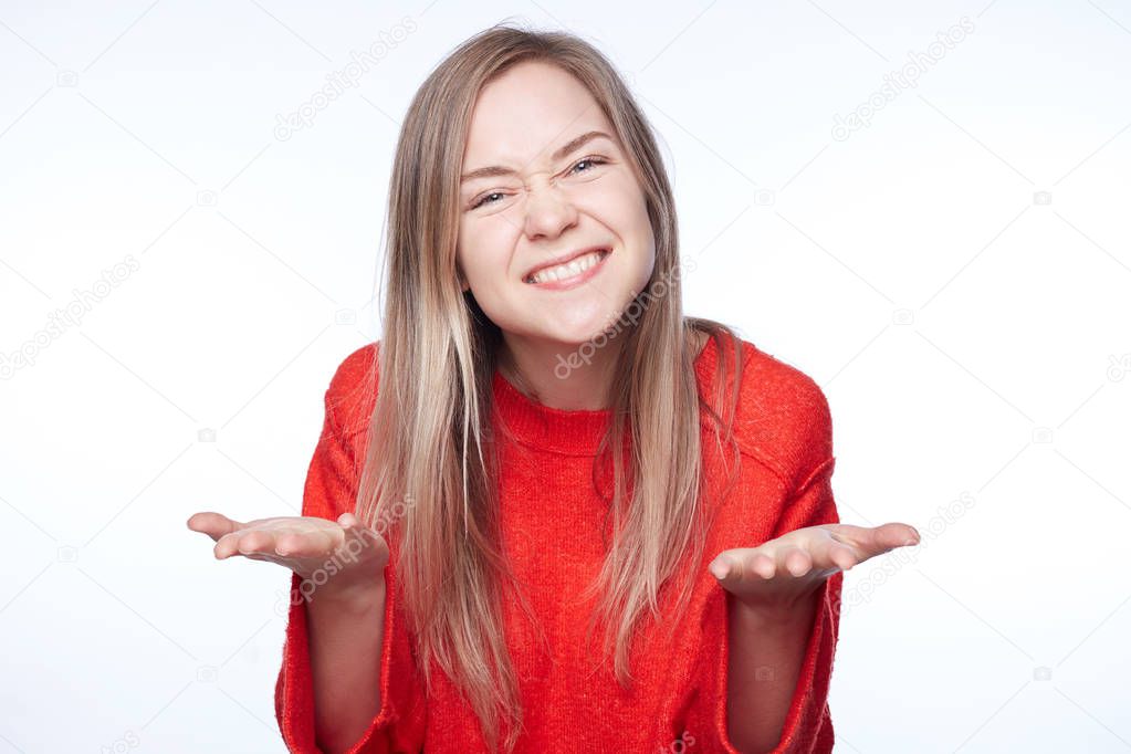 Blonde pretty female has long straight hair, gestures in happiness, meets with group mates after graduating from university, exchange news with each other. Happy attractive teenager poses indoors.