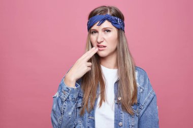 Güzel hippi Bayan pozlar pembe duvara hasta ediyor ve yorgun jest, ifade sıktı, şık kafa bandı, büyük boy kot ceket giyer. Negatif insan duygular, beden dili kavramı.