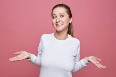 Kararsız güzel memnun Genç beyaz kadın omuz silkiyor, onu seçim yapmak ve nereye gideceğini, pembe studio arka plan üzerinde izole karar. İnsan duygu ve ifadeler kavramı.