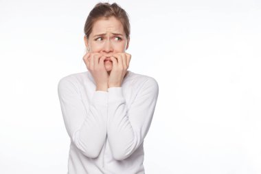 Beyaz stüdyo duvardan poz duygu tırnaklarını ısırma ve çevresinde korku, endişe ve sinir, ayakta dik korkmuş şirin güvensiz ve kadın ile sarı saçları gri gözler, portresi korkuttu.