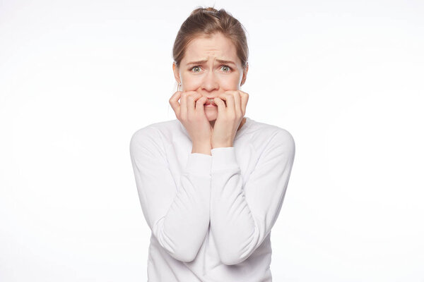 Woman is very terrified, trembling from fear. Portrait of attractive blond European female, biting fingernails and frowning, being worried and nervous, seeing something scary over white background.