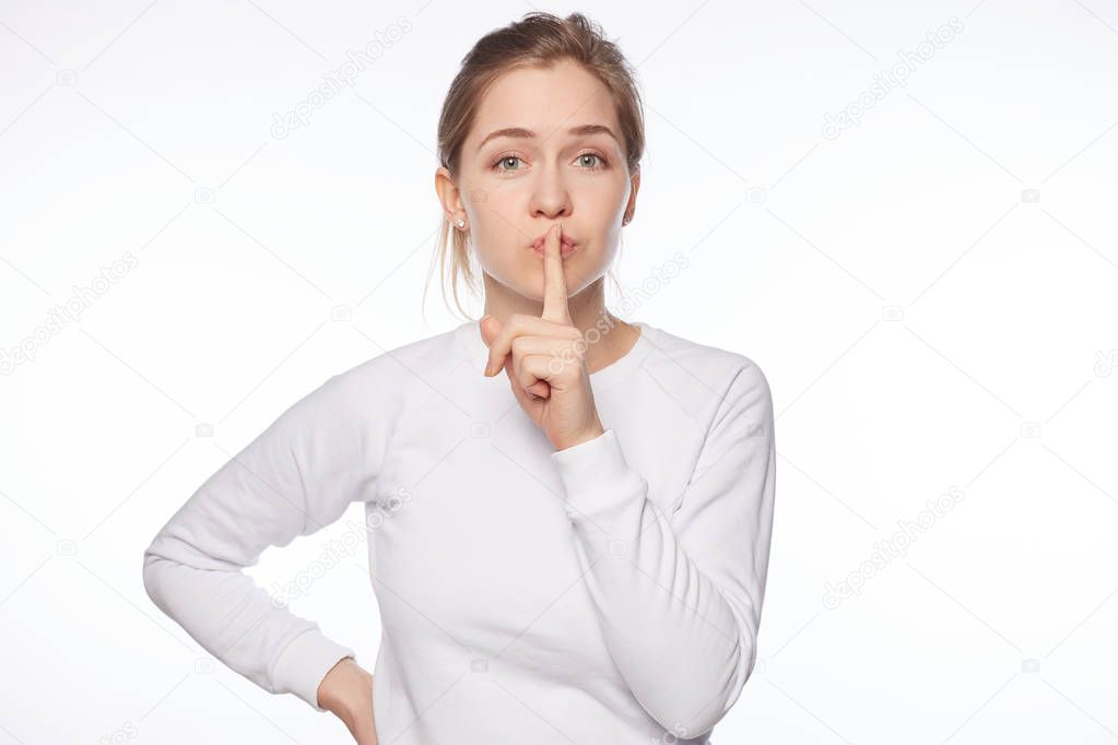 Keep our little secret. Feminine tender Caucasian woman with hair bun, saying shh while showing shush gesture with index finger over mouth, being mysterious or asking silence, telling keep voice down.
