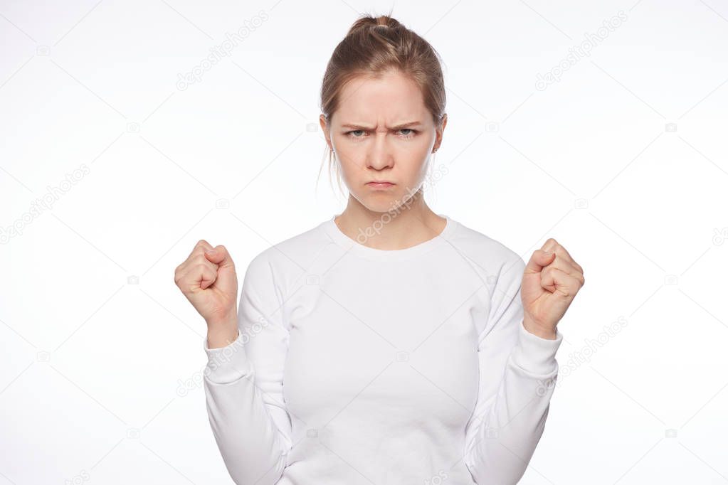 Offended European lady looking cute when angry. Portrait of outraged tender feminine woman, raising clenched fists and frowning, being insulted or mad, sulking from unhappiness over white background.