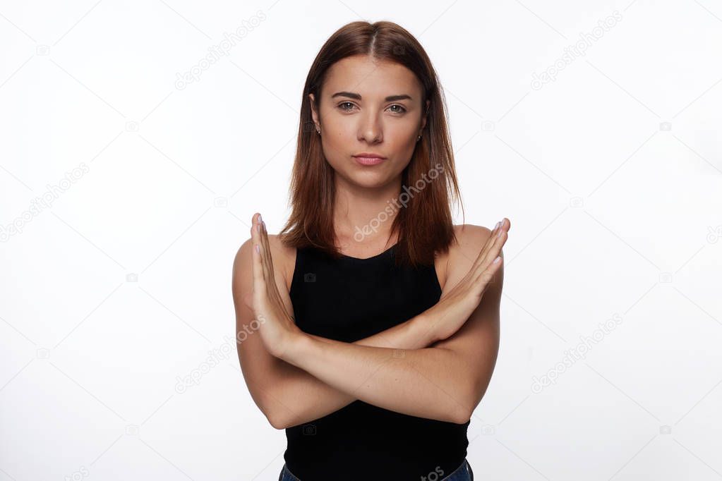 Suspicious  woman shows stop gesture, crosses hands, asks not to bother , isolated over white background with copy space for advertisement or promotional text. Grumpy female refuses to do something.