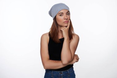 Güzel kadın, somurtkan ifade tutar parmak çene altında kasvetli görünüm vardır, bir şey üzerinde konsantre olmaya çalışır, şapka ve üst ve denim, giyer vardır dövme, kopya alanı ile beyaz arka plan üzerinde izole.