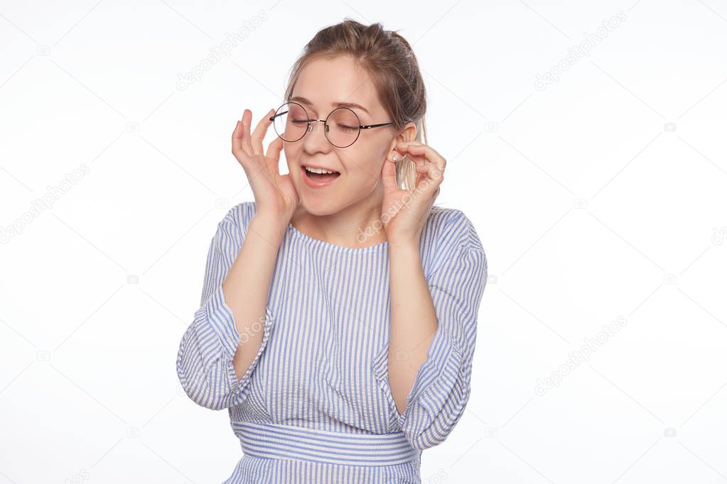 Young woman plugging ears with fingers , wearing round spectacles, does not want to listen loud music. European female ignoring noise or din covering ears with hands avoiding loud sounds at street.