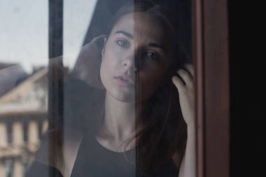 Kamerayla iletişim kirli pencereden bakarak Genç korkmuş Bayan şehvetli otantik portresi. Gerçek hayat ve sanat kavramı. İnsani duygular, duygular ve ifadeler doğal koşullarda.