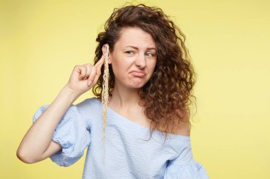 Do not pull my leg. Young beautiful Caucasian female wearing blue blouse, having curly bushy hairstyle and noodles on ear, listening to parter and not believe, feeling cheated,making grimace. clipart