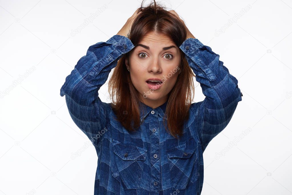 Young woman screaming in terror with hands on head, mouth wide open looking in panic at camera. Close up portrait of irritated female shouting, covering head, worrying about failure, isolated on white