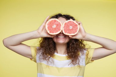 İzole yarıya portakal gözlerine tutan genç kıvırcık saçlı kadın portresi kapatın. Komik kız giyiyor headshot T-shirt pozlar sarı duvar şerit. İnsan yüz ifadeleri ve duygular. 