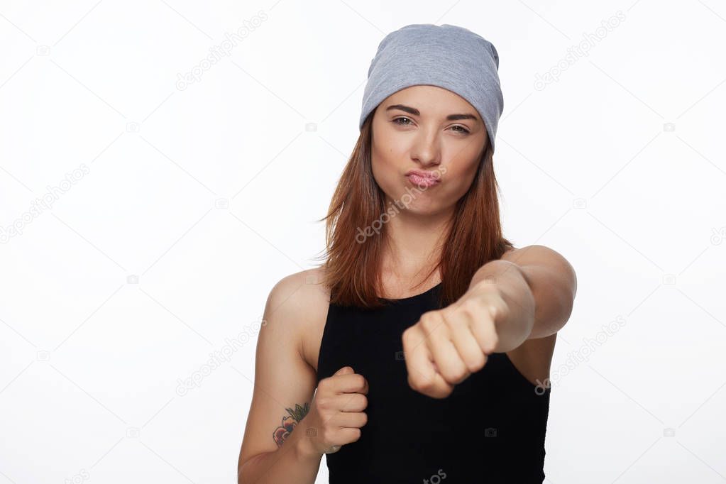 Defend and protection concept. Strong sporty woman wearing casual grey hat, having foxy and confident look, keeping fists clenched in front of her defending herself from jealous girls and bad eye.