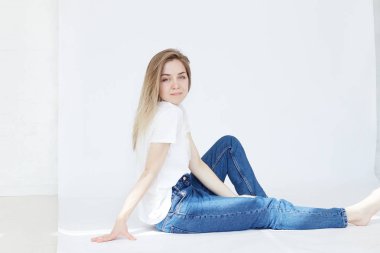 Uzun sarı saçlı beyaz stüdyo duvar arka plan kopya alanı için reklam, zevk serbest zaman, süre ile katta oturan şık kot giyen genç hipster kadın rahat hissediyor.