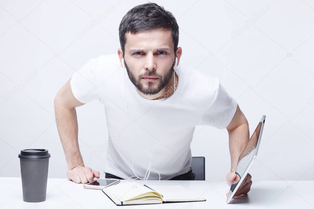 Hey you, listen to me! What did you say? Serious brutal male with worried expression suspects partner in cheating, attracts somebody`s attention, surrounded by gadgets in white office background.