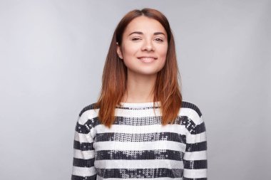 Çok gülümseyen sevinçle Fuarı saçlı kadın giyinmiş kayıtsızca, memnuniyeti kamera ile seyir, mutlu olmak. Stüdyo çekim yakışıklı güzel kadının boş gri studio duvara karşı izole.