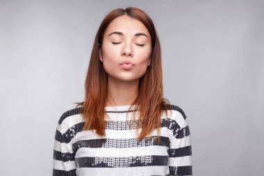 Kamera, mesafe, kapanır gözler, birinde öpecek güzel çekici kadın Gücenmek dudağı casual elbise, gri bir arka plana dayanır pozlar giymiş hoş görünümü vardır. İnsan yüz ifadeleri
