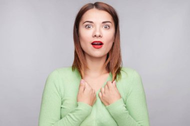 Dinleme cihazı gözlü müthiş kadın Kızıl saçlı, dokunmadan çilli deri, ağız yaygın, yeşillik kaşmir giyinmiş, kırmızı ruj giyer, gri bir arka plana dayanır son haberleri şok, standları açar.