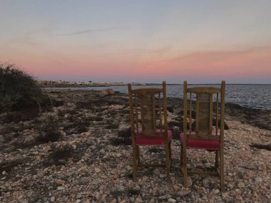 Romantik günbatımı tiyatro. Sinema gökyüzü altında. Akdeniz'in güzel manzaranın tadını ziyaretçiler için bekleyen iki sandalye kayalık Plajı, pitoresk bir kadeh. Seyahat ve doğa kavramı.