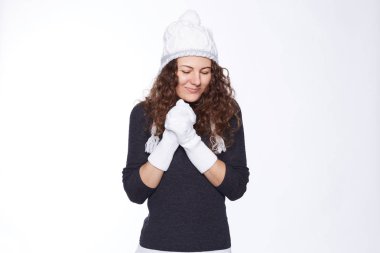 İnsanlar, iyilik ve cömertlik kavramı. Sıcak giyimli genç güzel kadın şapka ve eldiven eller kalp üzerinde tutar, samimiyet ve dostu ifade eder, gülümseme yakışıklı yakaladı, stüdyo duvara pozlar.