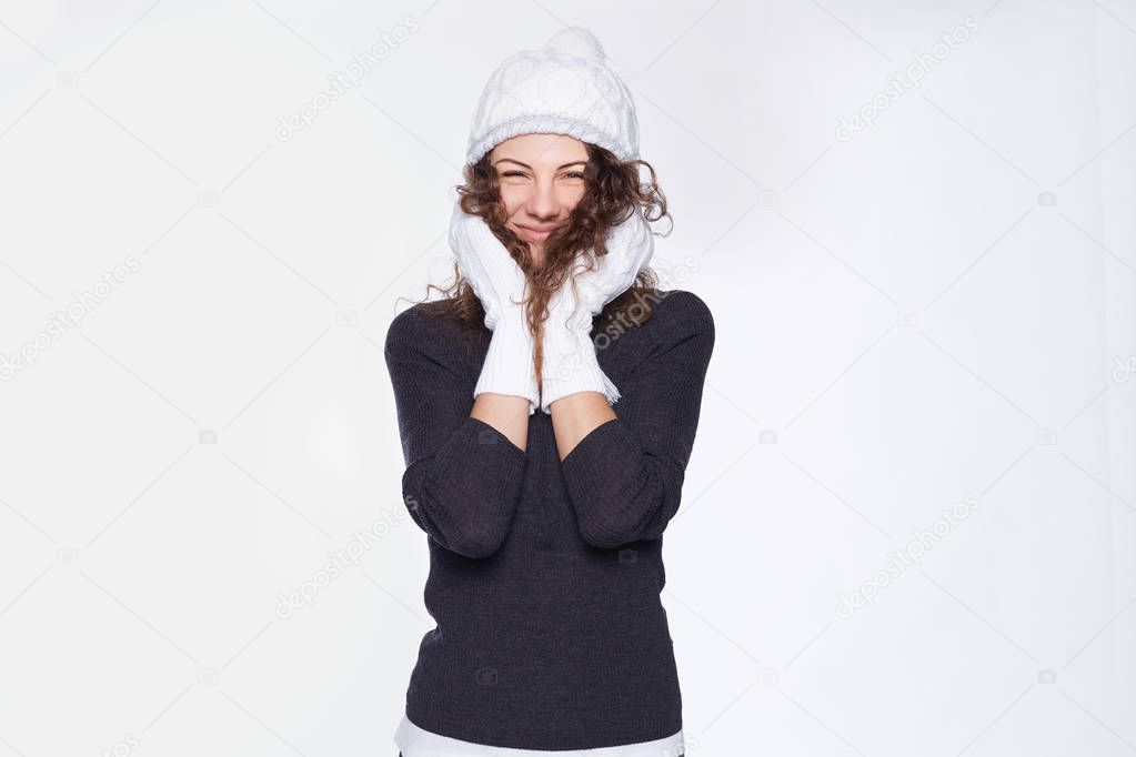 Winter is coming! Pretty Caucasian fashionable lady felling happy about final seasonal sale in favorite shop, dressed in new brand accessories, ready for cold times, posing on white studio blank wall.