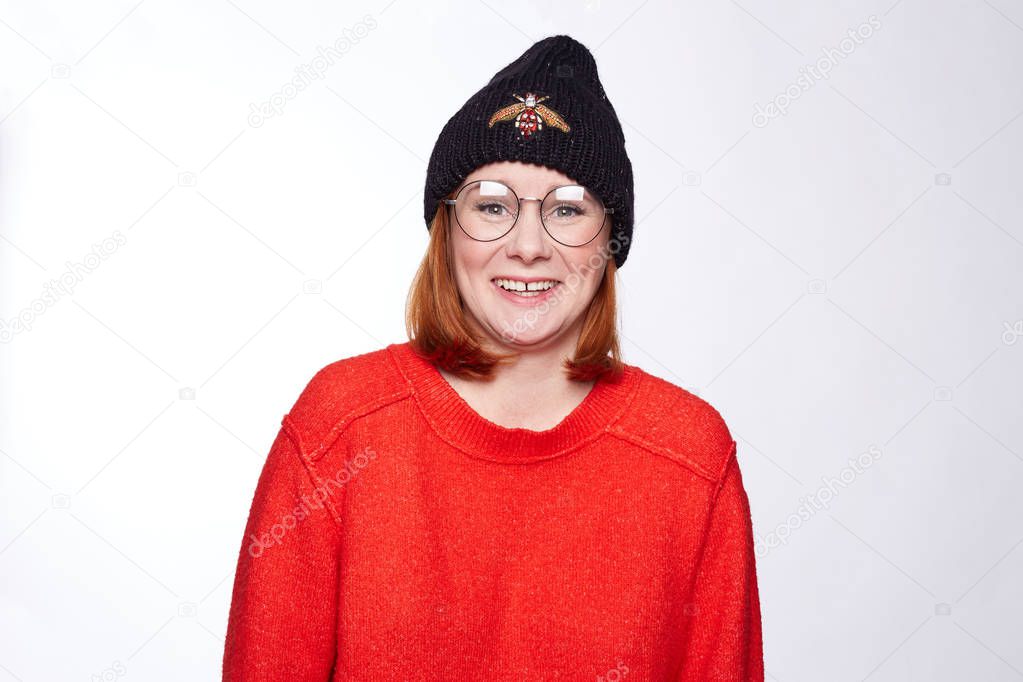 Human facial expressions, emotions and feelings. Portrait of funny funky teenage hipster lady wearing stylish knitted hat and sweater, having happy look, laughing at camera, posing at blank white wall 
